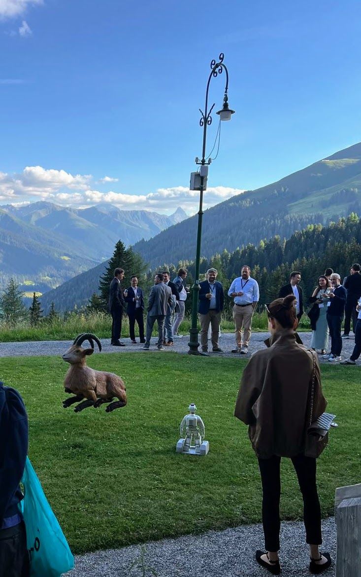 A humanoid robot on the lawn beside the ibex sculpture at the Davos Tech Summit evening reception, with the Grisons mountains behind